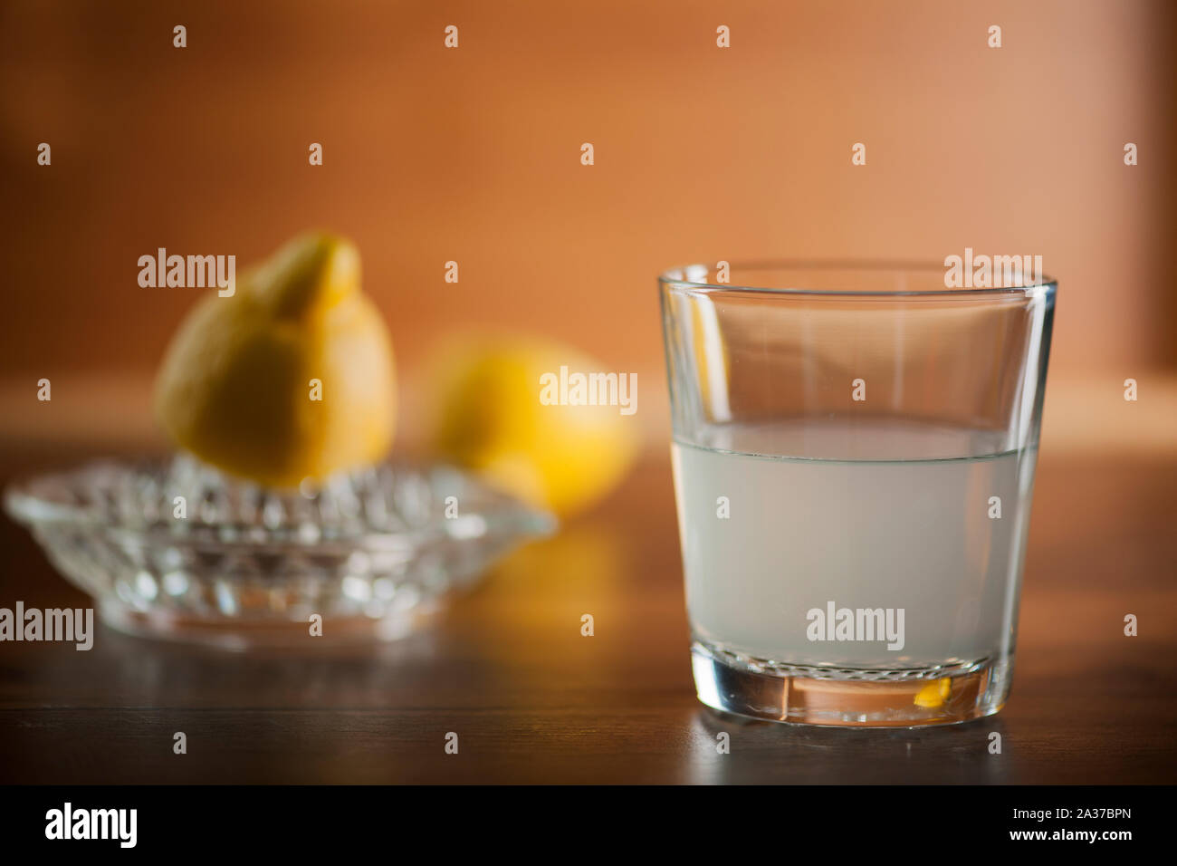 Spremuta di succo di limone in un bicchiere sul tavolo di cucina con piastra dimezzato i limoni e di limone in spremitore sfondo sfocato. Foto Stock