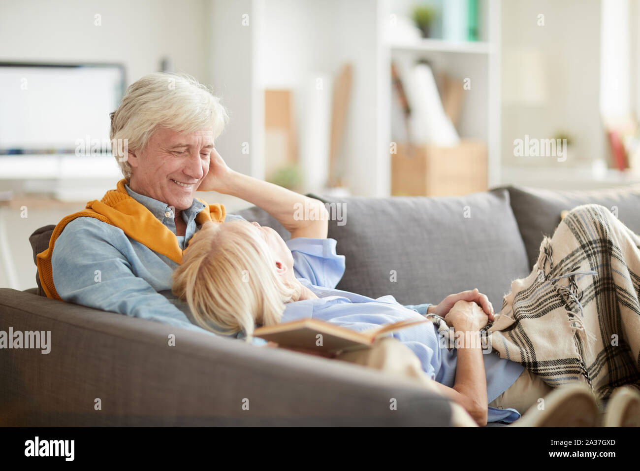 Ritratto di felice coppia senior godendo il tempo libero insieme sdraiati su un comodo divano a casa, spazio di copia Foto Stock
