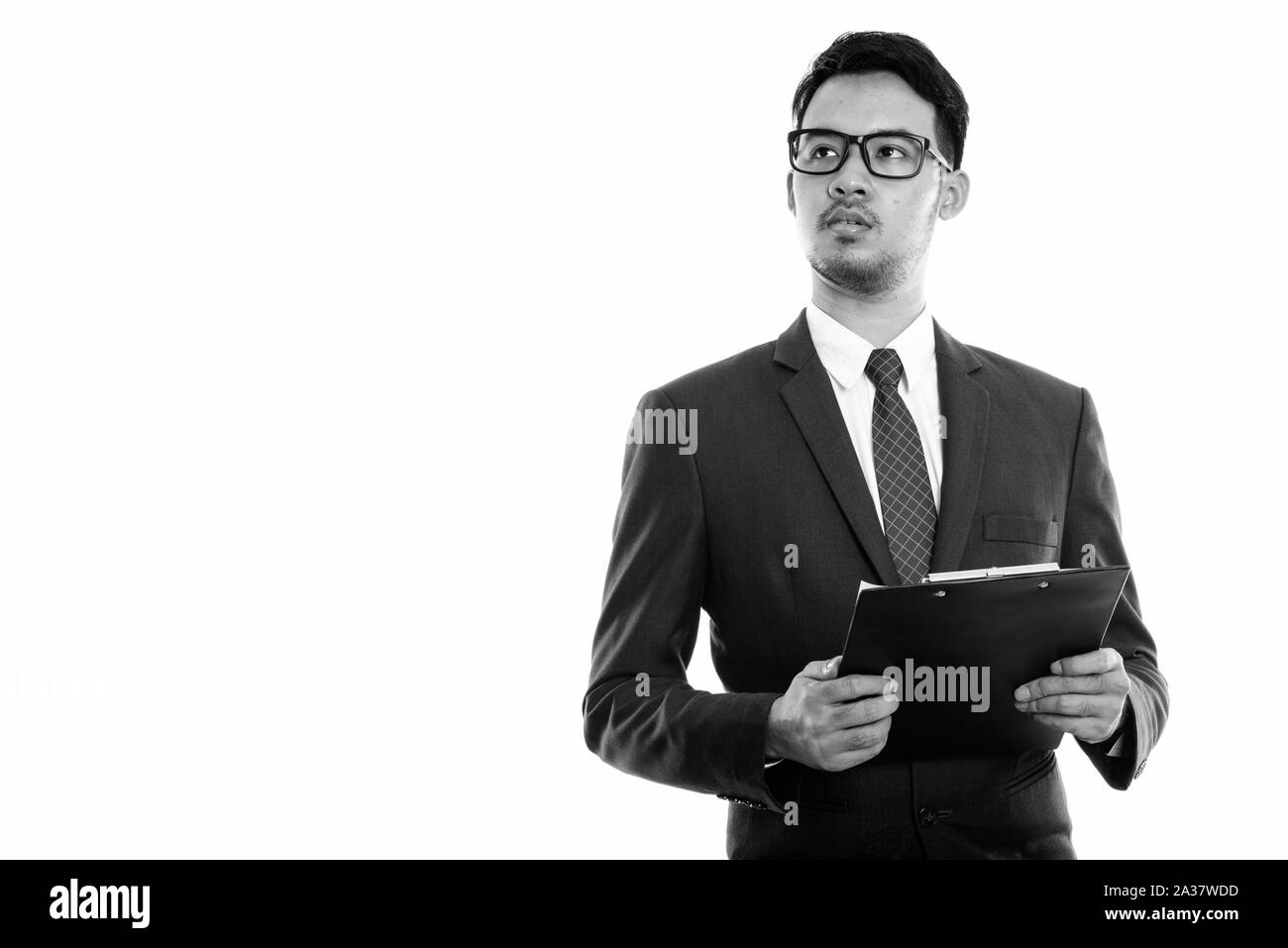Studio shot del giovane imprenditore asiatici holding clipboard mentre pensando Foto Stock