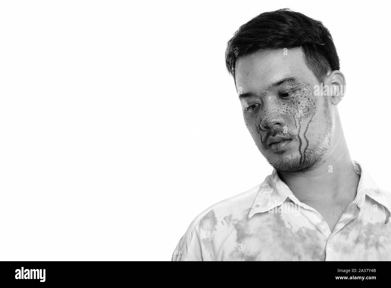 Studio shot di giovani pazzo uomo asiatico pensando mentre guardando verso il basso con il sangue sulla faccia Foto Stock
