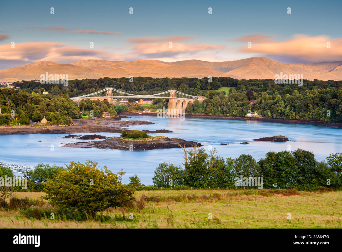 Una vista di Menai Bridge da Anglesey guardando attraverso il Menai Strait verso la terraferma del Galles e la gamma della montagna del Parco Nazionale di Snowdonia. Foto Stock