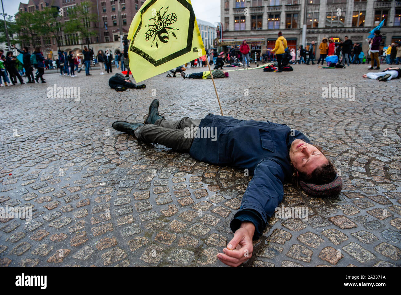 Un attivista del clima getta a terra mentre si tiene un flag durante le prestazioni.Prima della estinzione internazionale ribellione settimana inizia a Amsterdam, un gruppo di attivisti XR riuniti nel centro della città per fare un popolo con la dichiarazione di crisi climatica. Essi hanno anche eseguito un 'die-in-action", che coinvolge un gruppo di persone il montaggio in un luogo e far cadere morto a terra mentre vestito tematicamente e mantenendo una adeguata di poster e insegne. Foto Stock