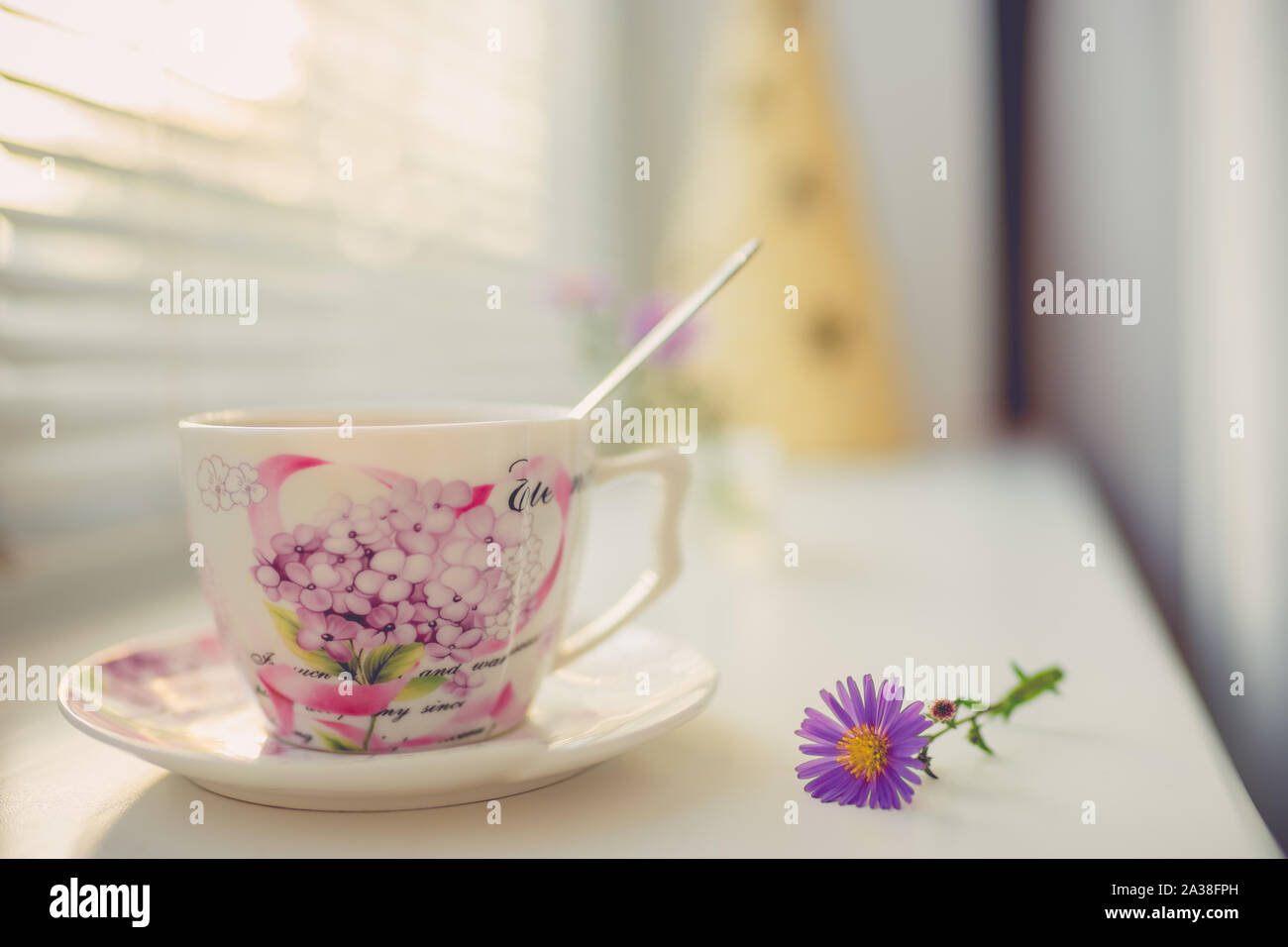 Vintage elegante tazza di porcellana e cucchiaio sul davanzale bianco, vista laterale con la calda luce del sole. Foto Stock