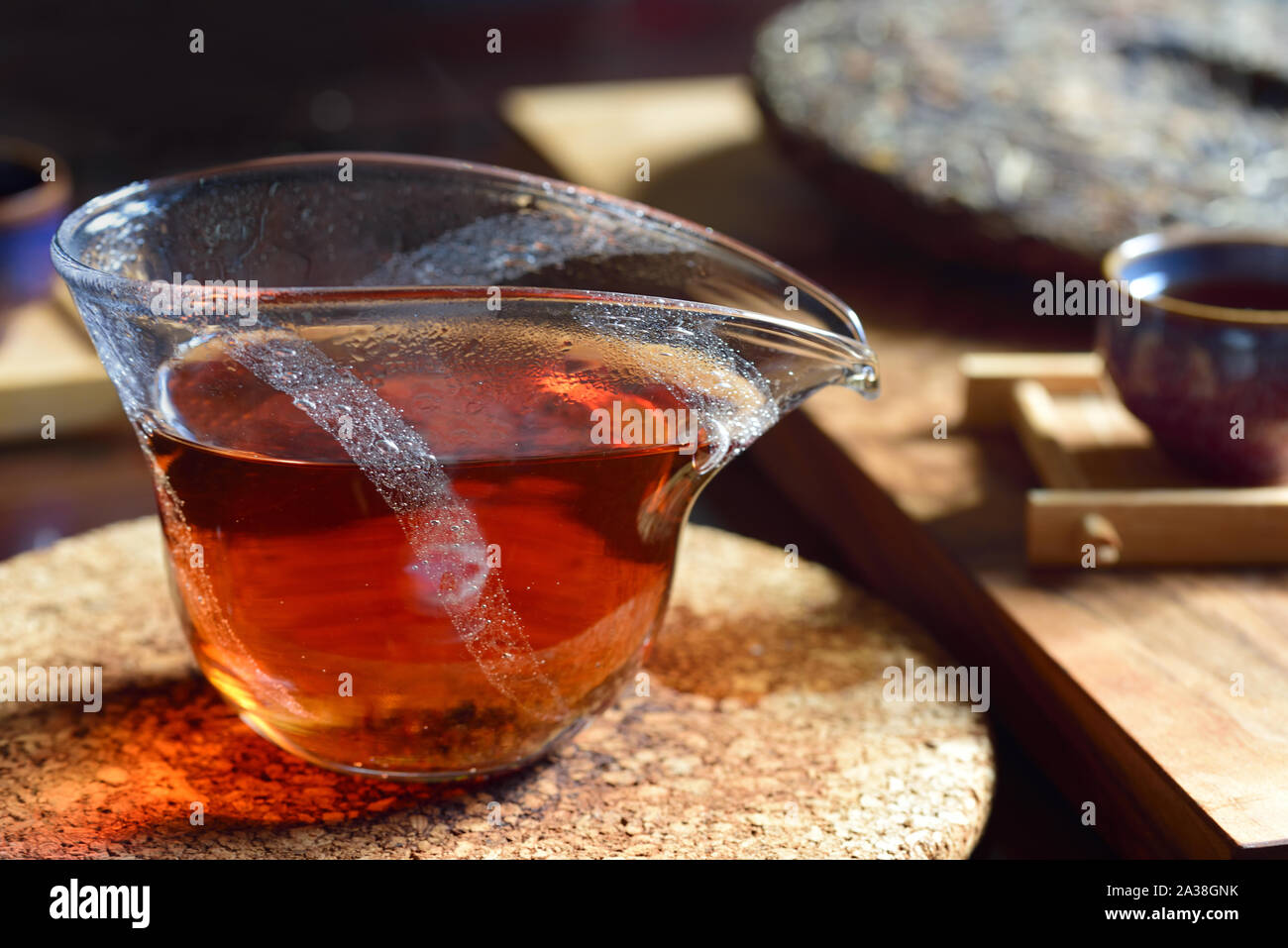 Tipica scena di una cerimonia del tè cinese con vetro teiera e caldo tè nero all'interno, tè pressato torta in background e un bicchiere su un tavolo scuro Foto Stock
