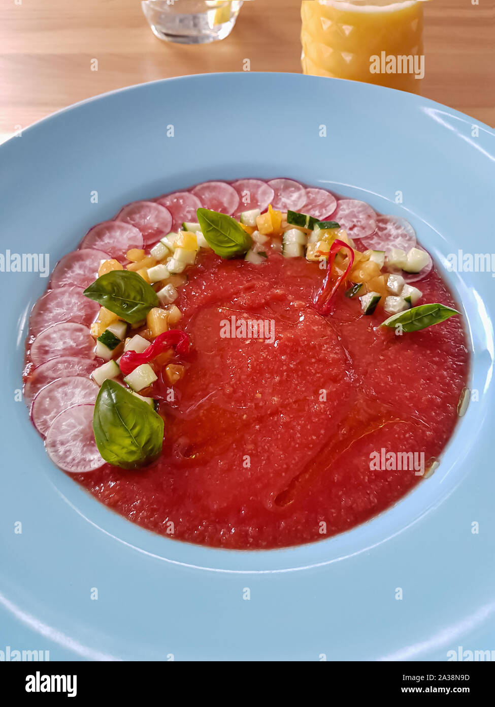 Ristorante spagnolo servita fresca zuppa gazpacho fatto di pomodori rossi, servita nella piastra bianca e decorate con fresche verdure colorate e basilico Foto Stock