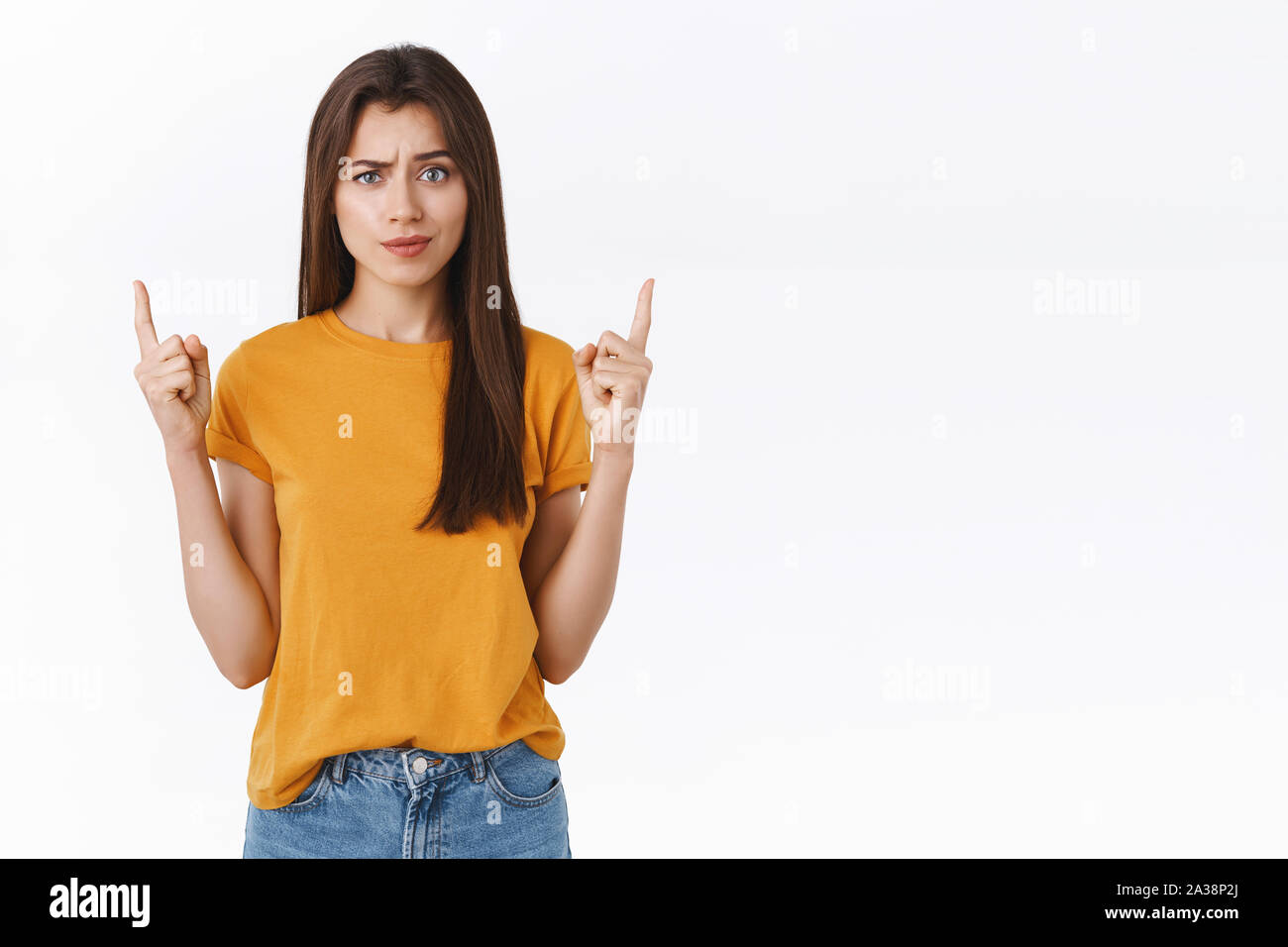 Scettici, sicuri e interrogato bella bruna donna in giallo t-shirt solleva un sopracciglio dubbioso, rivolto verso l'alto come aspetto leggermente la fotocamera Foto Stock