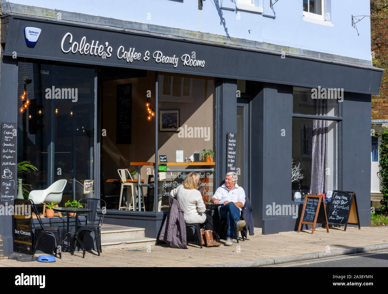 La mezza età matura gustare caffè al sole a Colette di caffè e stanze per trattamenti di bellezza, Bridge Street, Christchurch, Dorset, England, Regno Unito Foto Stock