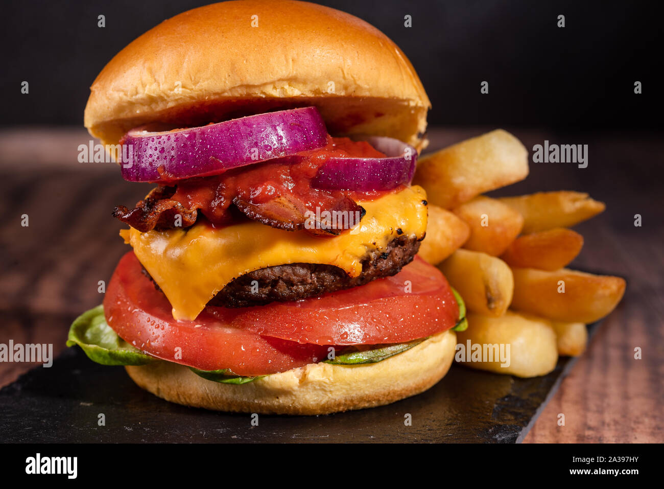 Bacon Cheeseburger con lattuga cipolla pomodoro su uno sfondo scuro e Brioche bun Foto Stock