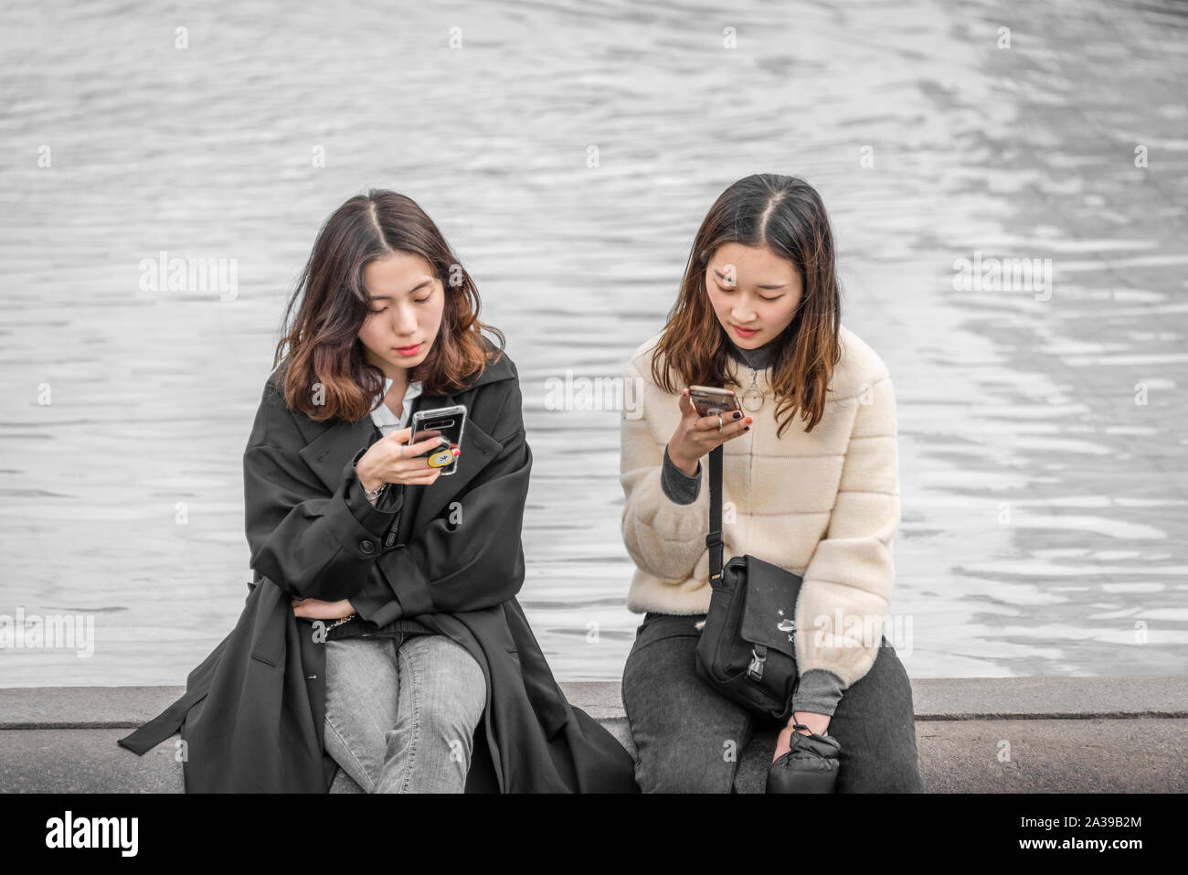 Due giovani ragazze controllare i loro telefoni cellulari mentre seduto sul bordo di una fontana in Trafalgar Square, Londra centrale. Foto Stock
