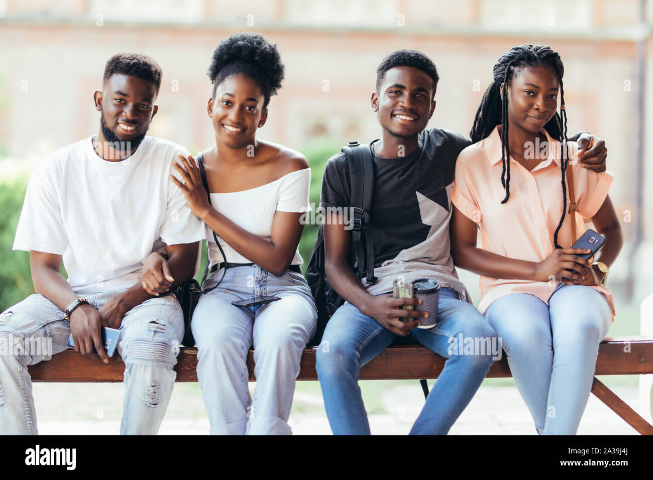 Un gruppo di giovani amici africani appendere fuori insieme all'aperto su un banco e ridere mentre discutono Foto Stock