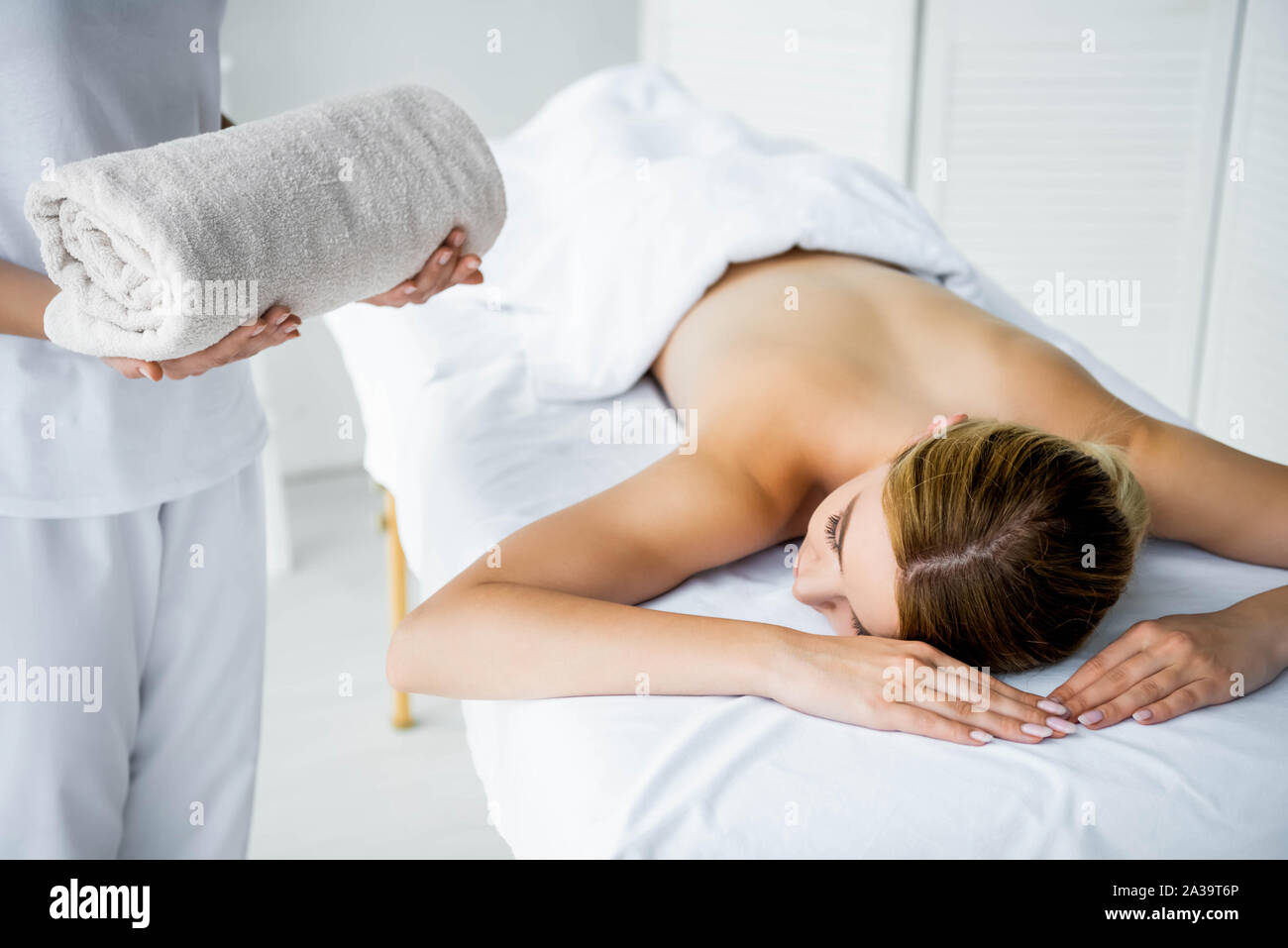 Vista ritagliata della massaggiatrice tenendo un asciugamano e donna sdraiata sul tappeto di massaggio Foto Stock