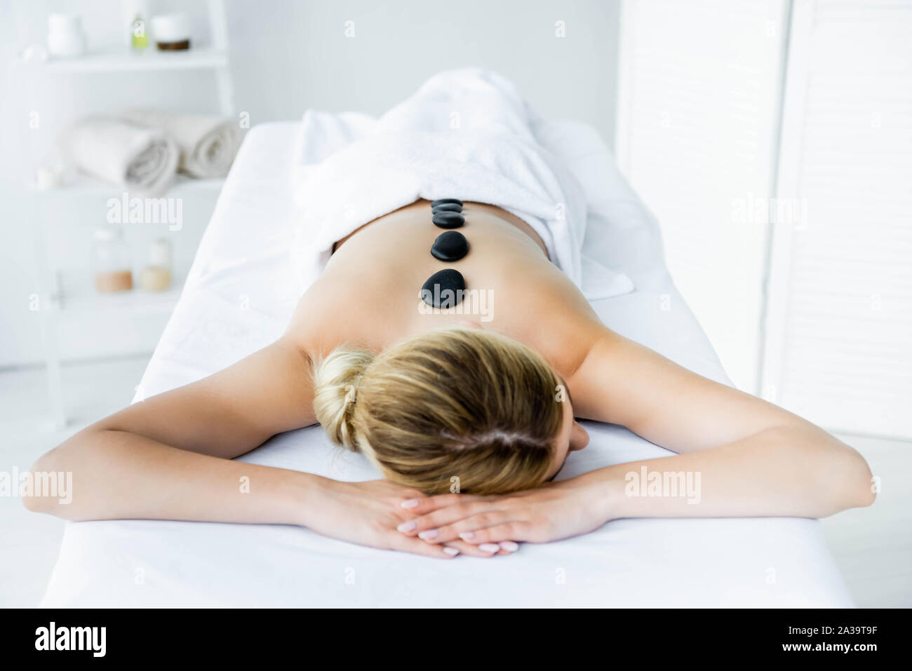Donna con pietre calde sul retro giacente sul tappeto di massaggio Foto Stock