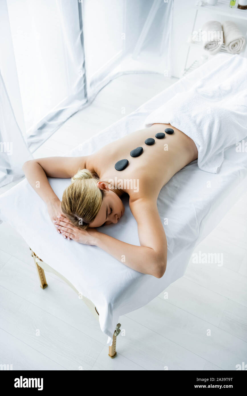 Elevato angolo di visione della donna attraente con pietre calde sul retro giacente sul tappeto di massaggio Foto Stock