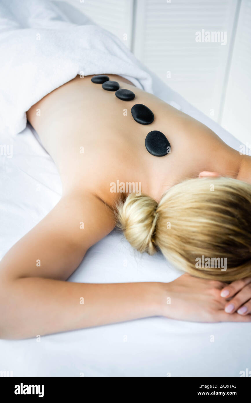 Donna con pietre calde sul retro giacente sul tappeto di massaggio Foto Stock