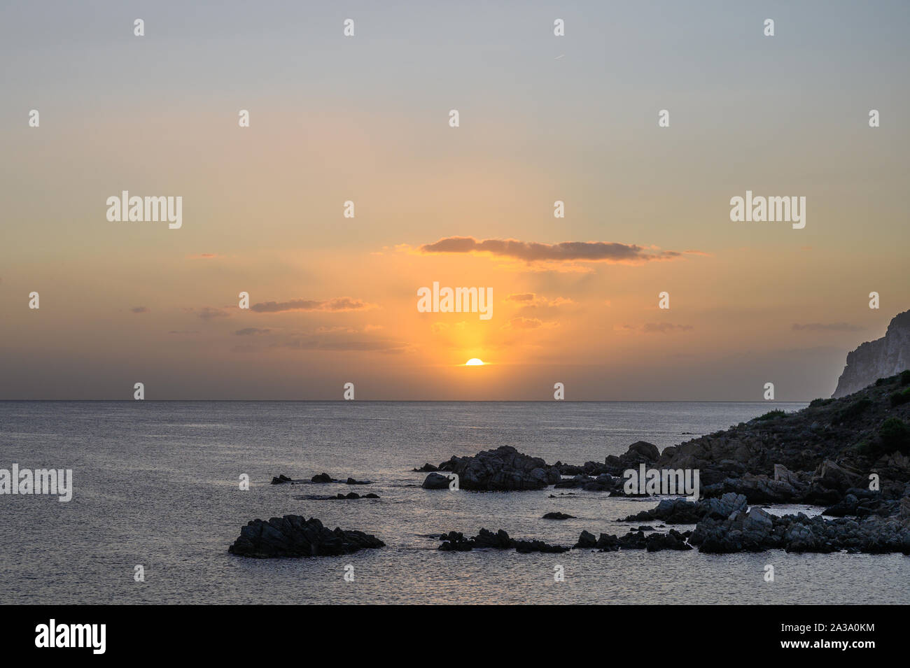 Alba sul mare. I raggi del sole si riflettono nelle nuvole. In primo piano una spiaggia rocciosa Foto Stock