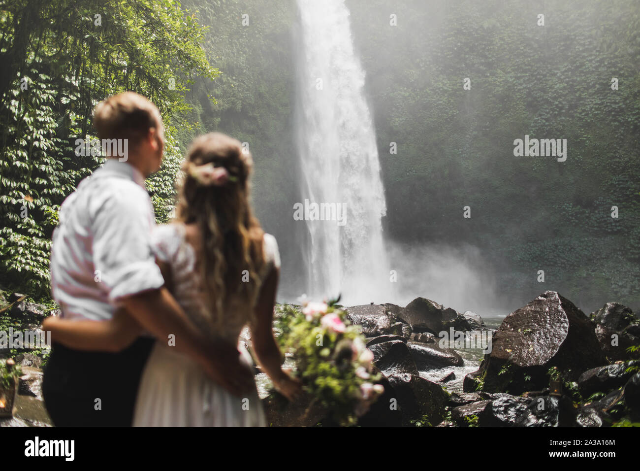 Coppie in viaggio di nozze in amore cerca su enorme cascata Nung-Nung in Bali Jungle. Nozze in Asia con una straordinaria vista della natura. Foto Stock