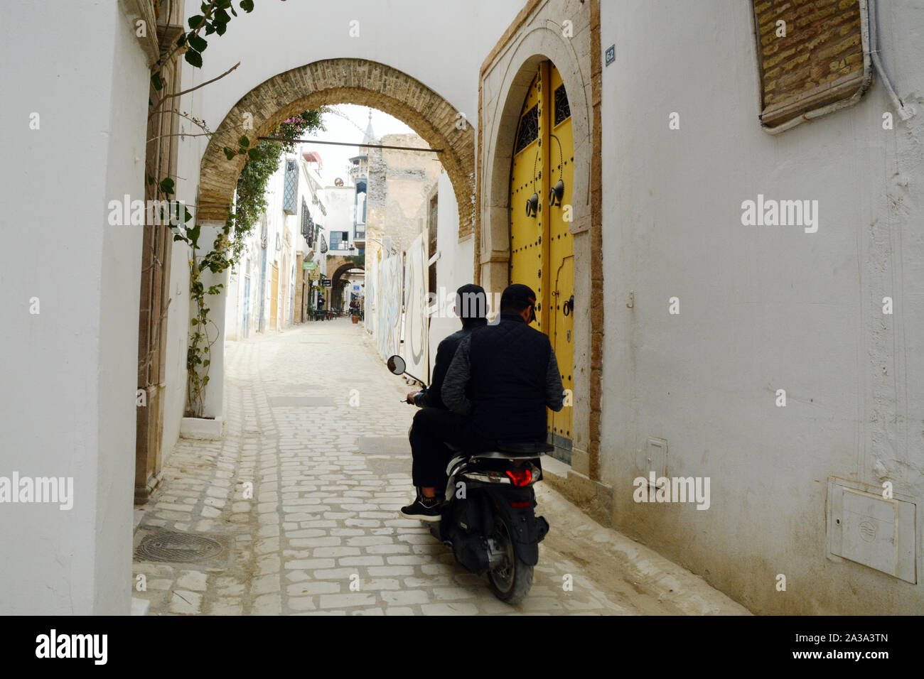Due giovani uomini tunisini in sella a una moto attraverso le strade pedonali del quartiere Hafsia della Medina (città vecchia) di Tunisi, Tunisia. Foto Stock
