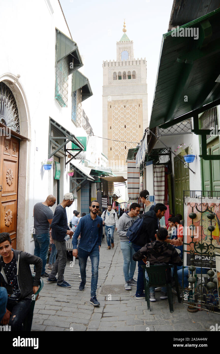 La gente in un vicoletto pedonale nel cuore della medina (città vecchia) di Tunisi con il quadrato minareto della moschea Zeitoun visto in background, Tunisia. Foto Stock