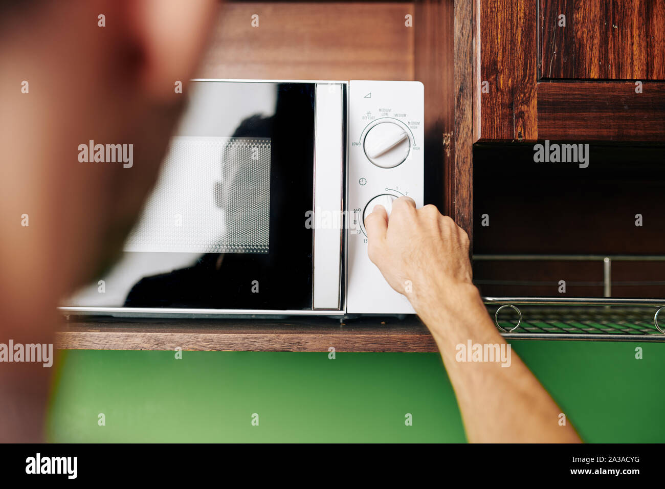 Uomo che utilizza un forno a microonde per riscaldare il cibo per la cena, vista dal retro Foto Stock