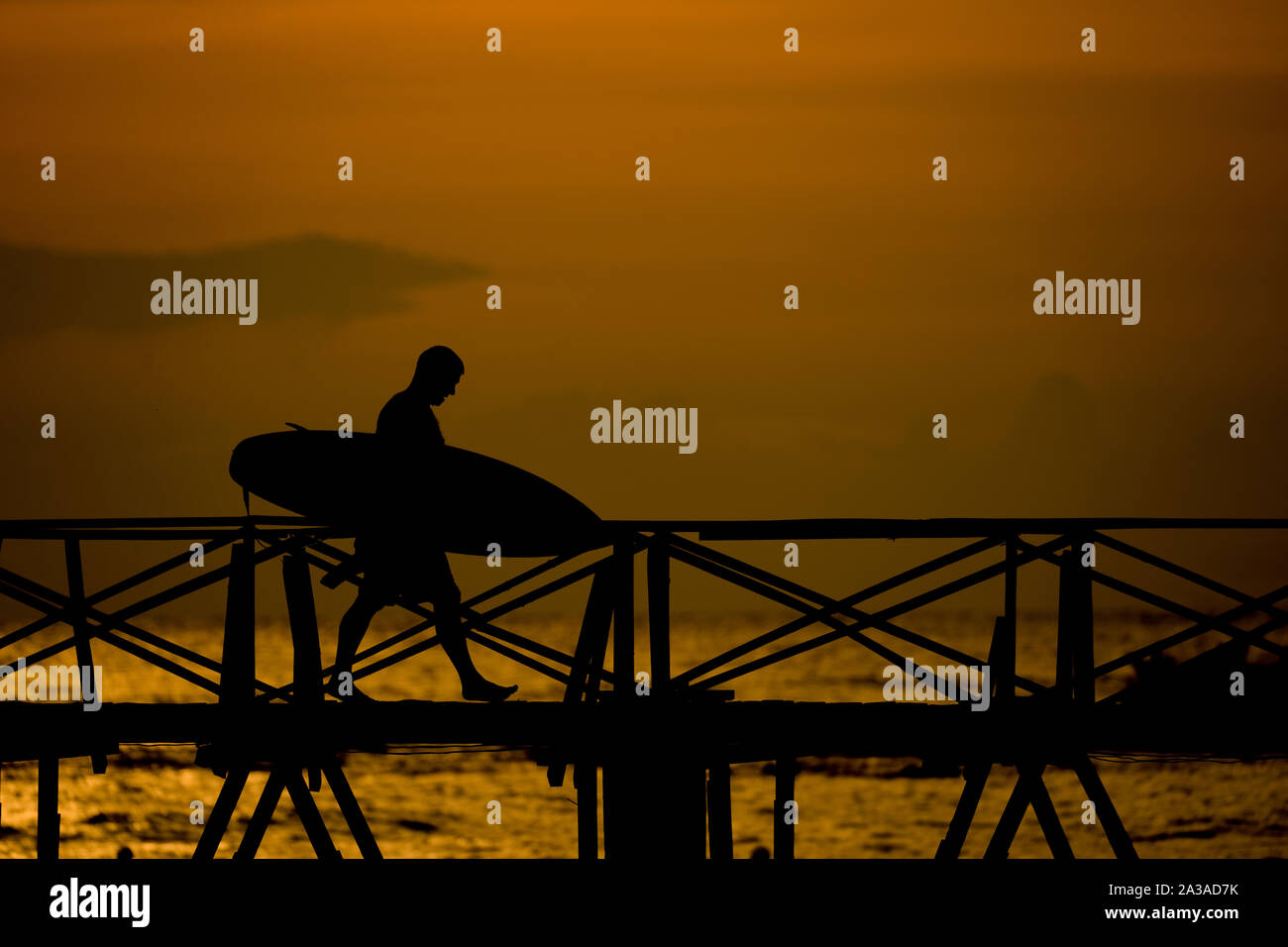 Lo spuntar del giorno come un surfista maschio passeggiate lungo la passeggiata a mare dalla zona di surf del Cloud 9,Siargao,Filippine Foto Stock