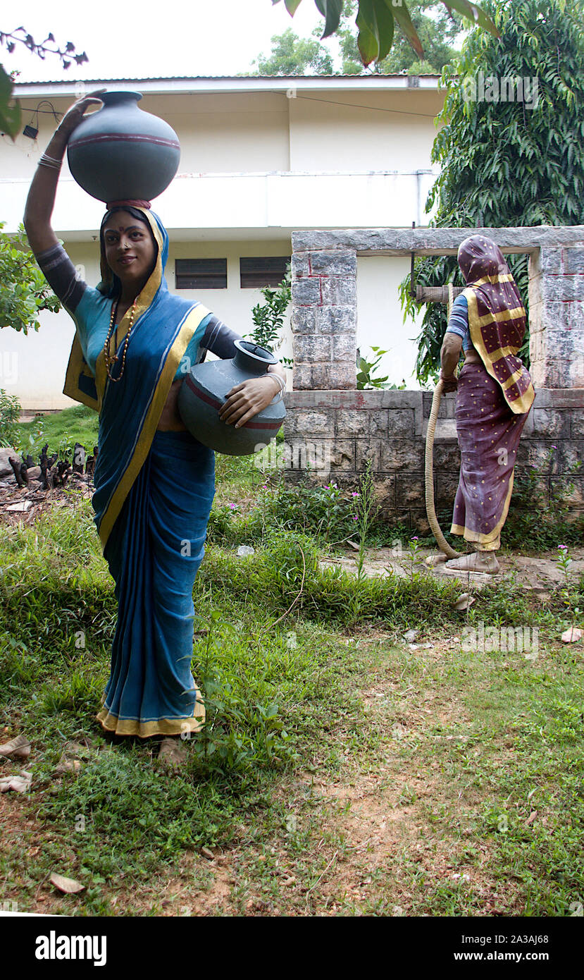 Vista del villaggio di due donne, uno riempimento di acqua dal bene e l'altro recando vasi d'acqua, a Janapada Loka Folk Art Museum vicino Ramanagara, Karnataka, Foto Stock
