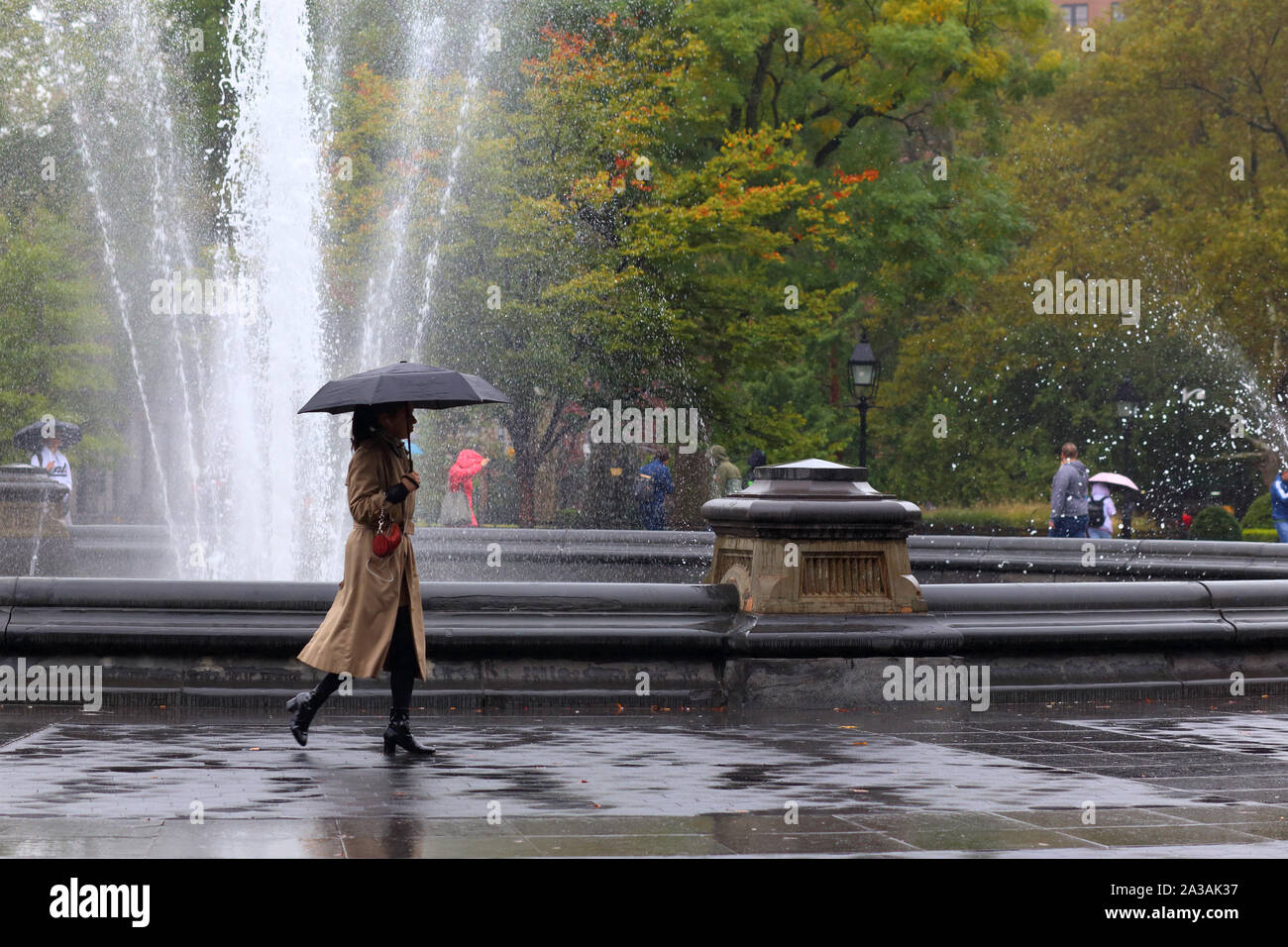 Una donna con un ombrello da passeggiate Washington Square Park fontana su un drizzy, Rainy day in New York City Foto Stock
