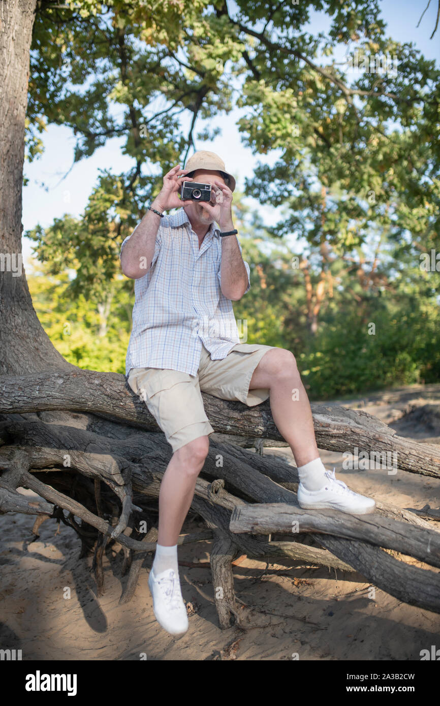 Uomo che indossa estate hat usando la sua macchina fotografica durante la cattura la natura Foto Stock