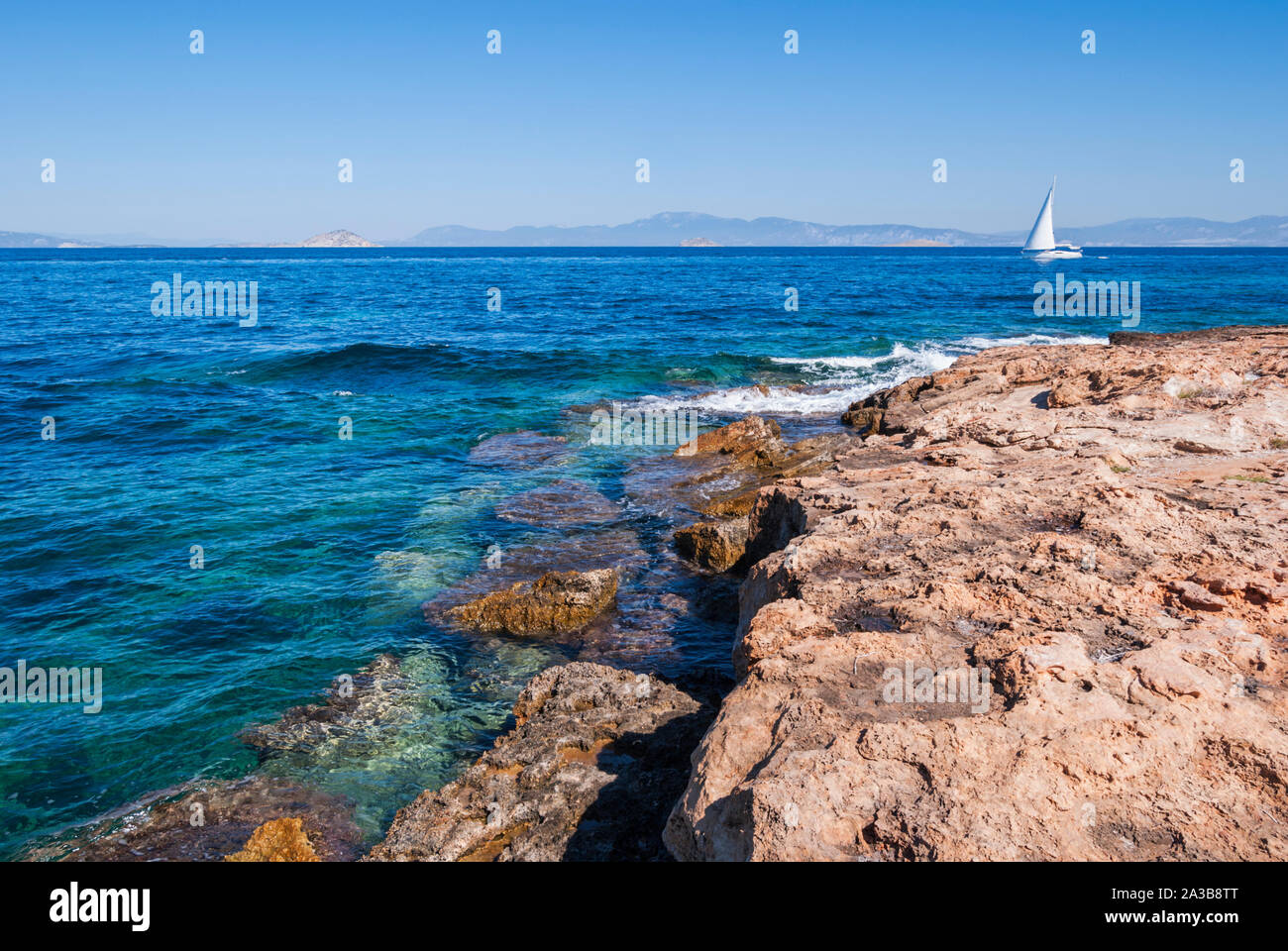 Uno yacht a vela passa vicino a una costa rocciosa Foto Stock