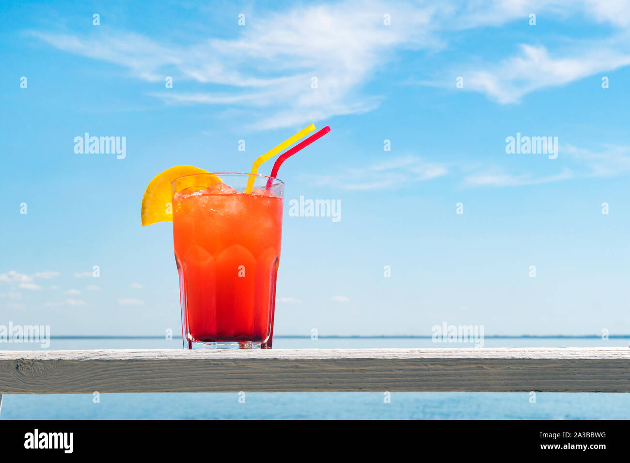 Bocal di cocktail alla frutta su una spiaggia tabella. un bicchiere di rosso di succo di frutti di bosco con una cannuccia e una fetta di arancia sul tavolo di legno in un bar in riva al mare. su b Foto Stock