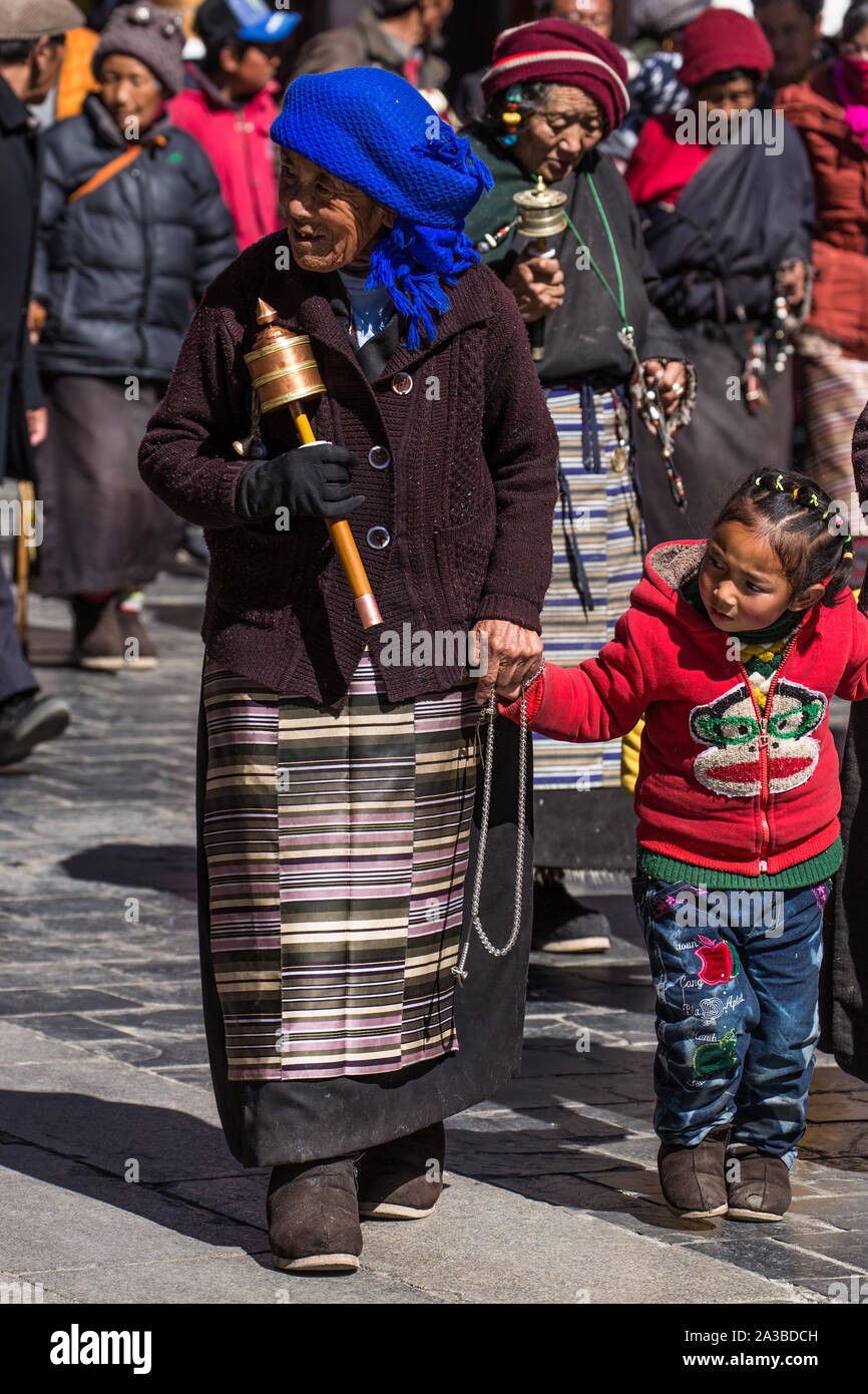 Un Buddista nonna e la nipote circumambulate il tempio del Jokhang a Lhasa, in Tibet. Ella porta una ruota di preghiera e di mala i grani del rosario. Foto Stock