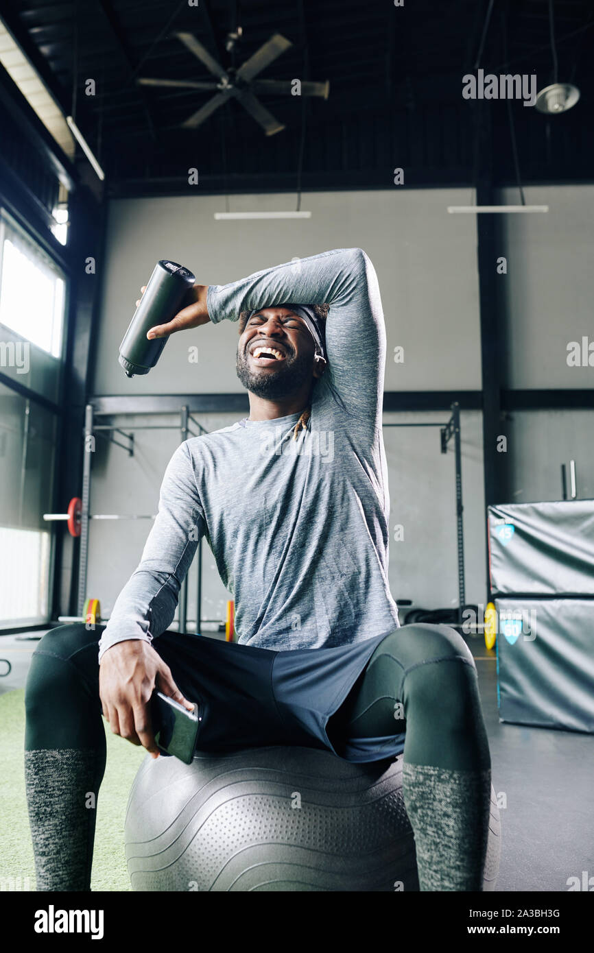 Stanchi ma felici sportsman tergi sudore della fronte fronthis quando in appoggio sulla sfera fitness dopo esercizio in palestra Foto Stock