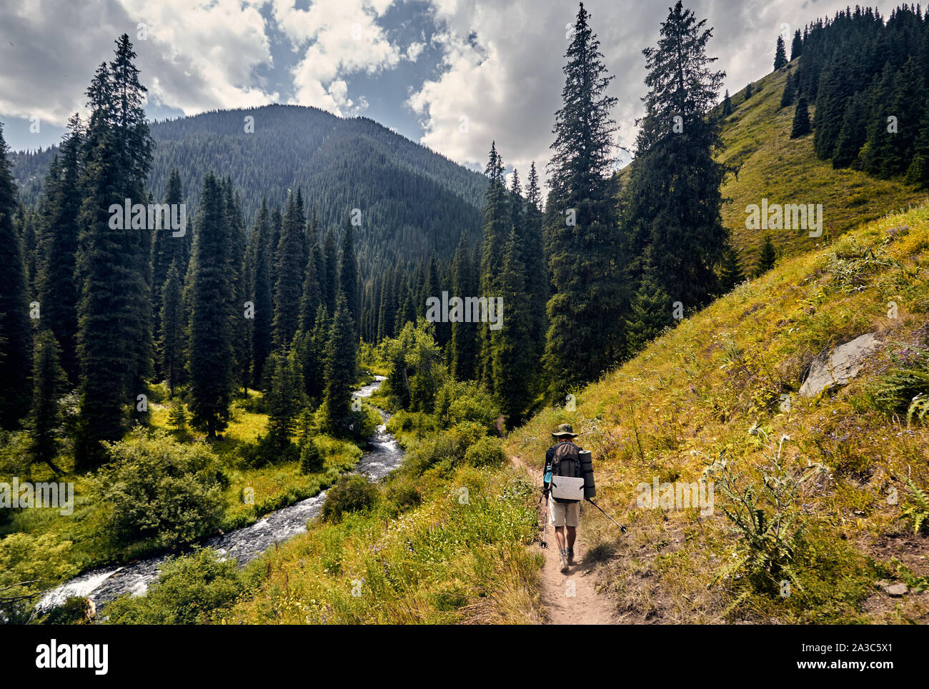 Escursionista con grande zaino è di camminare sulla strada con una vista spettacolare delle montagne e del fiume Foto Stock