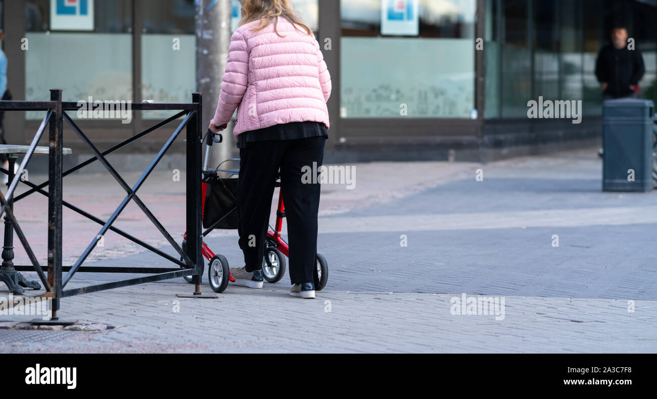 La persona disabile utilizzando un telaio a piedi per la stabilità in una strada urbana visto dal retro con spazio di copia Foto Stock