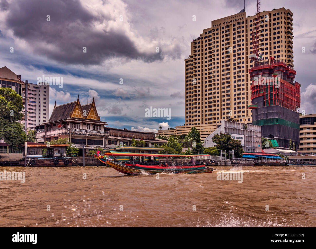 Di una barca dalla coda lunga velocità lungo il Fiume Chao Phraya a Bangkok in Tailandia. In fondo è un edificio tradizionale e alcuni edifici modernissimi. Foto Stock