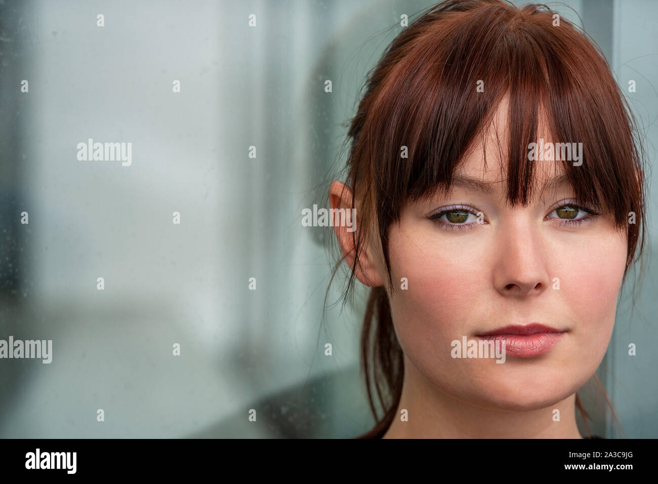 Bella triste premuto o riflessivo femmina ragazza giovane donna nel suo ventenne seduta da una pioggia finestra coperto con le riflessioni di un corridoio Foto Stock