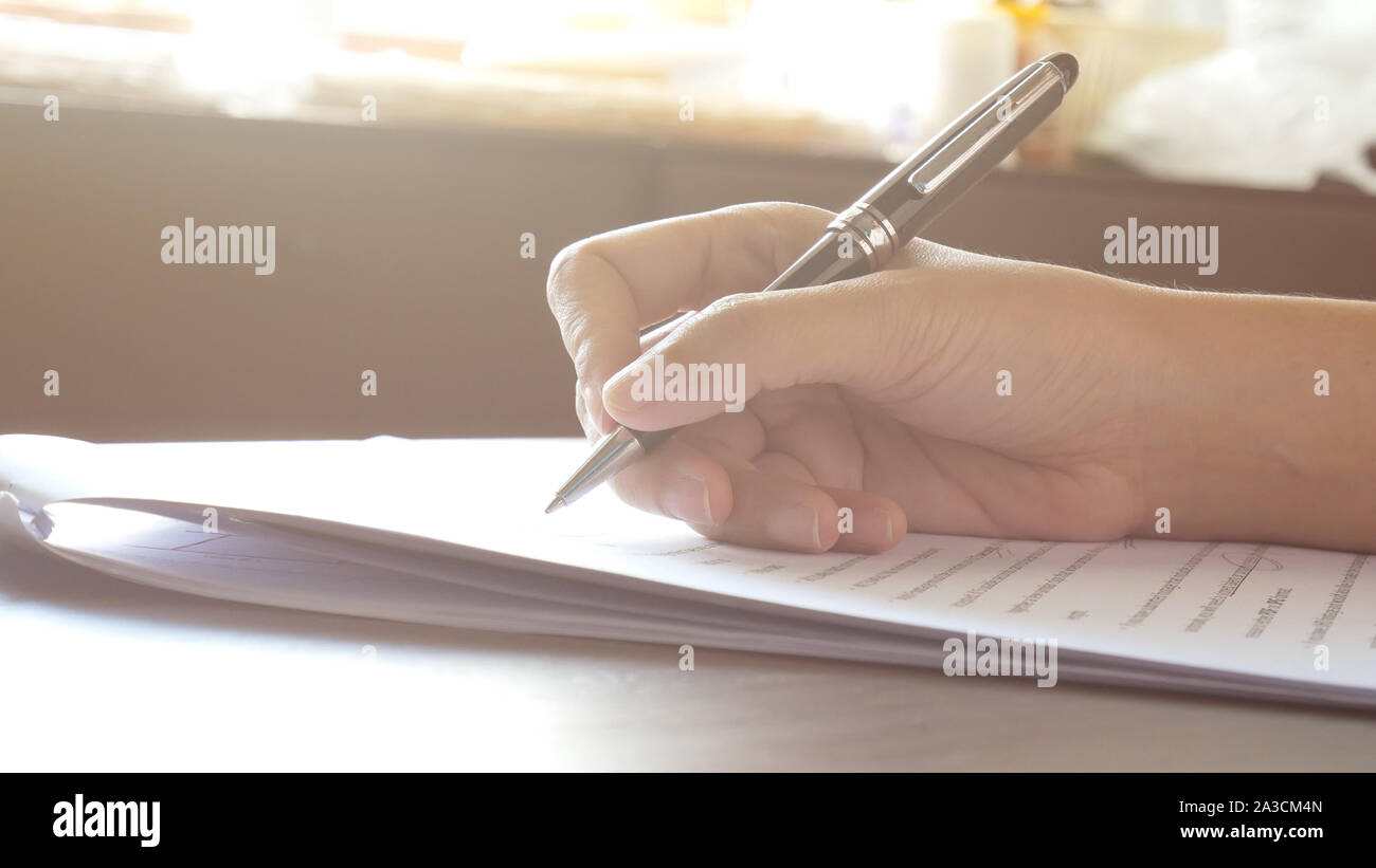 Close up donna mani di firma o la scrittura di un documento su un foglio di carta bianca con la penna nera al mattino Foto Stock