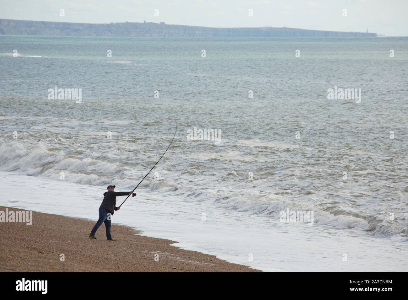 Un pescatore gettata su Chesil Beach in ottobre il giorno dopo una tempesta quando il vento è sceso con l'isola di Portland in background. La pesca Foto Stock