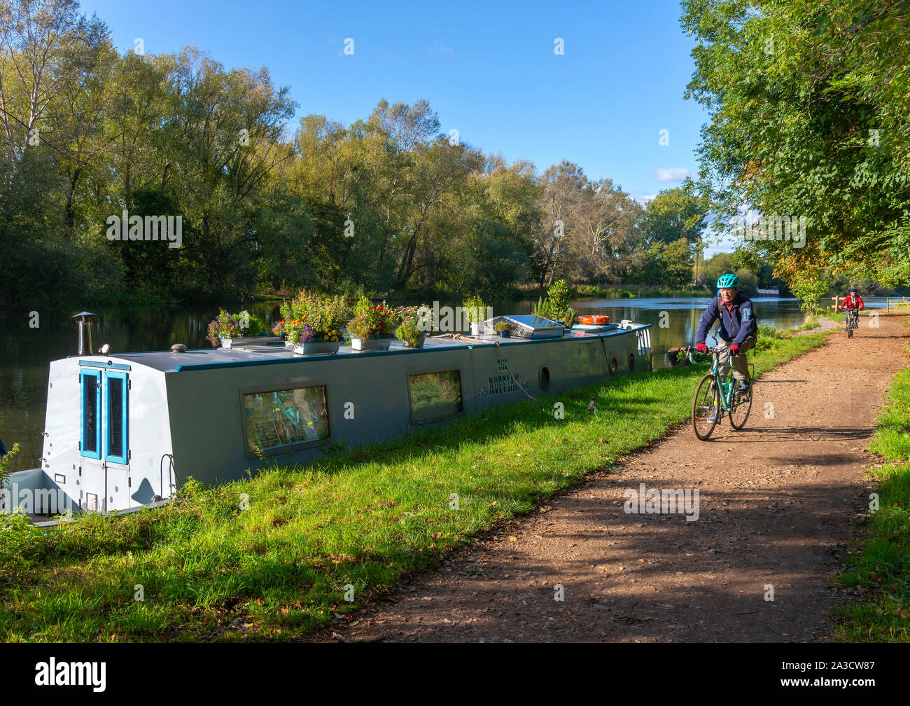 Gli uomini in bicicletta lungo il percorso del Tamigi passando una barca stretta in un pomeriggio autunnale accanto al Fiume Tamigi a Sonning on Thames, Berkshire, Inghilterra, Regno Unito Foto Stock