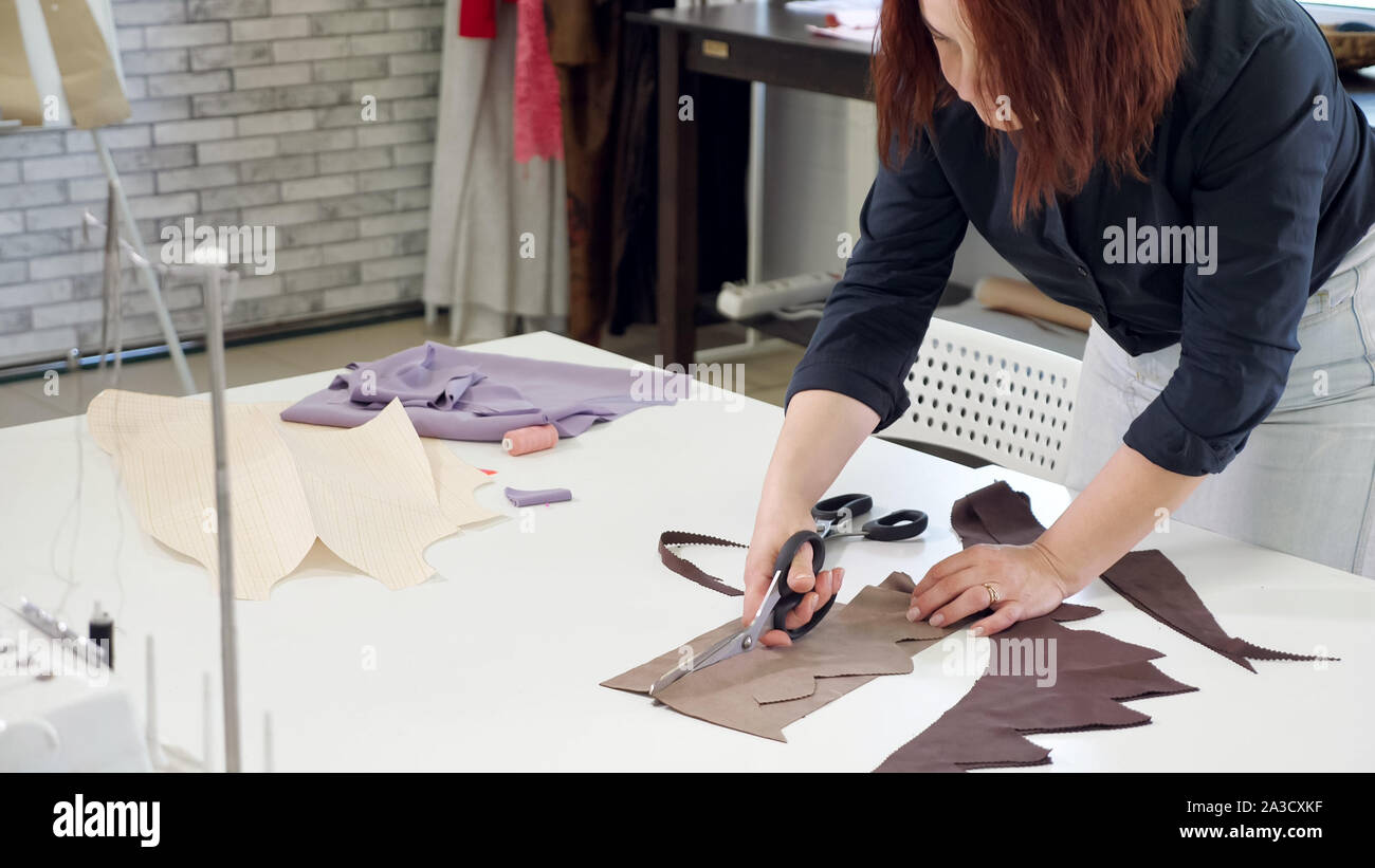 Taglio e cucito prodotti in sartoria aziendale. Adattare la donna i dettagli di taglio dal tessuto lavora in sartoria workshop aziendali. Il taglio con le forbici a zig-zag. Sarta la creazione di un nuovo prodotto. Foto Stock