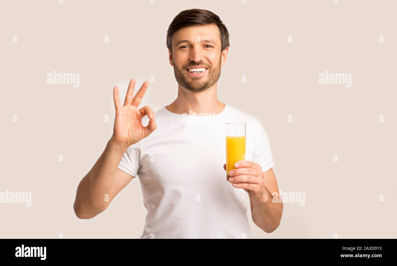 Positivo Uomo con vetro di succo d'Arancia gesticolando OK, sfondo bianco Foto Stock