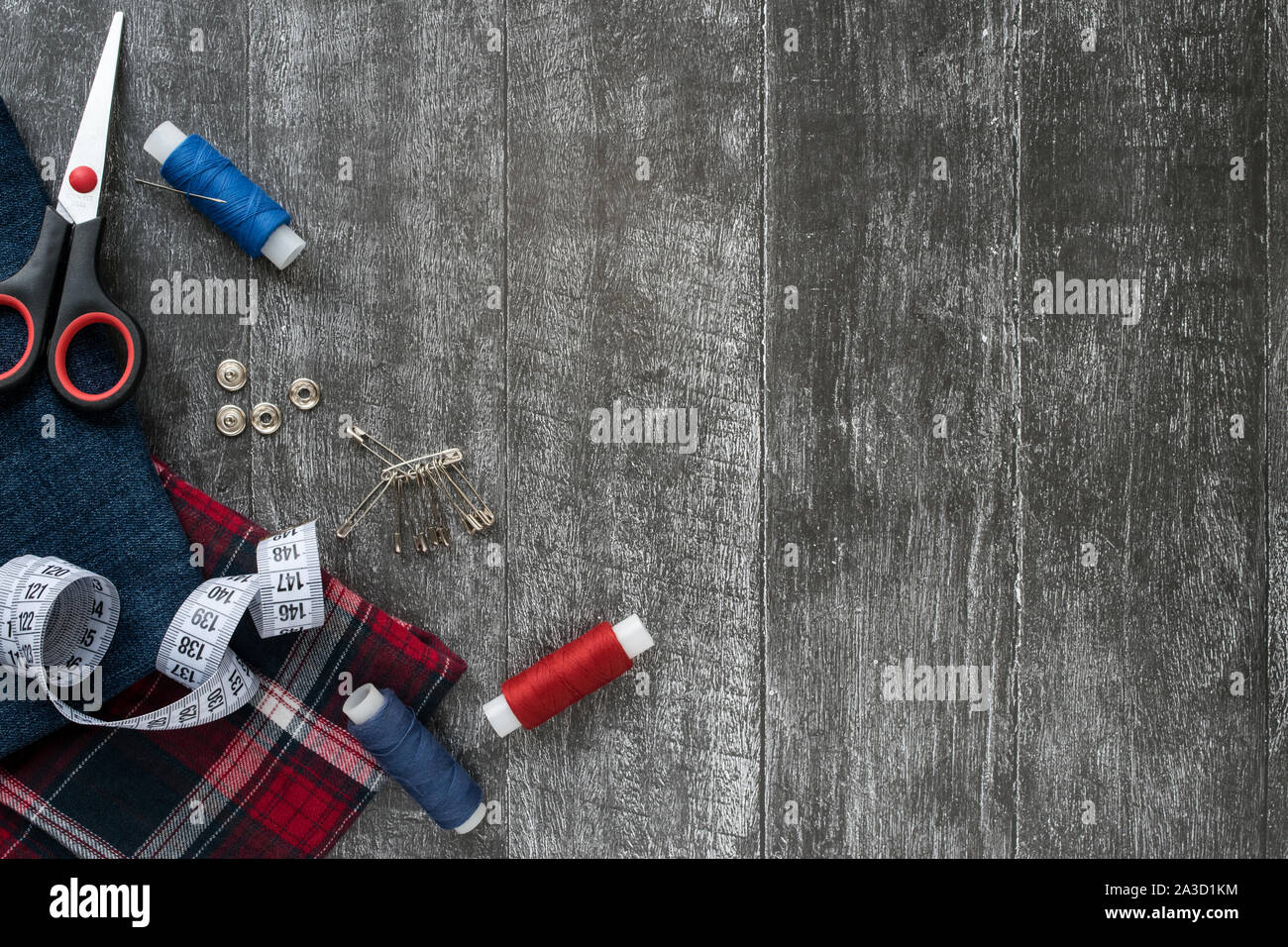 Accessori per il cucito, jeans e plaid tessuto su di un legno scuro dello sfondo. Tessuto, fili di cucitura, ago, spilli, forbici, pulsanti e centimetro di cucitura Foto Stock