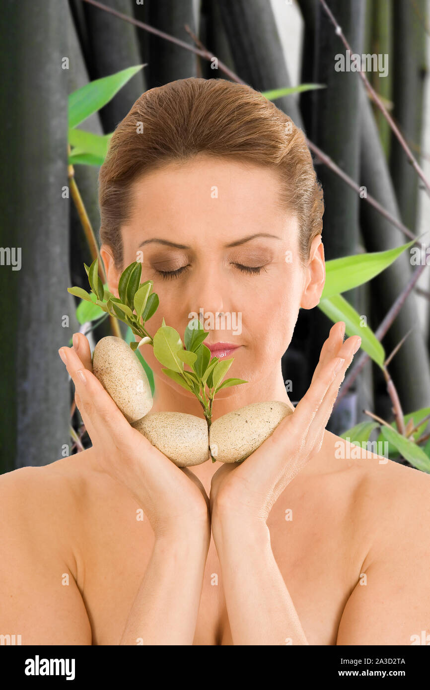 La donna rilassante con gli occhi chiusi, con ciottoli e un'erba in mano Foto Stock