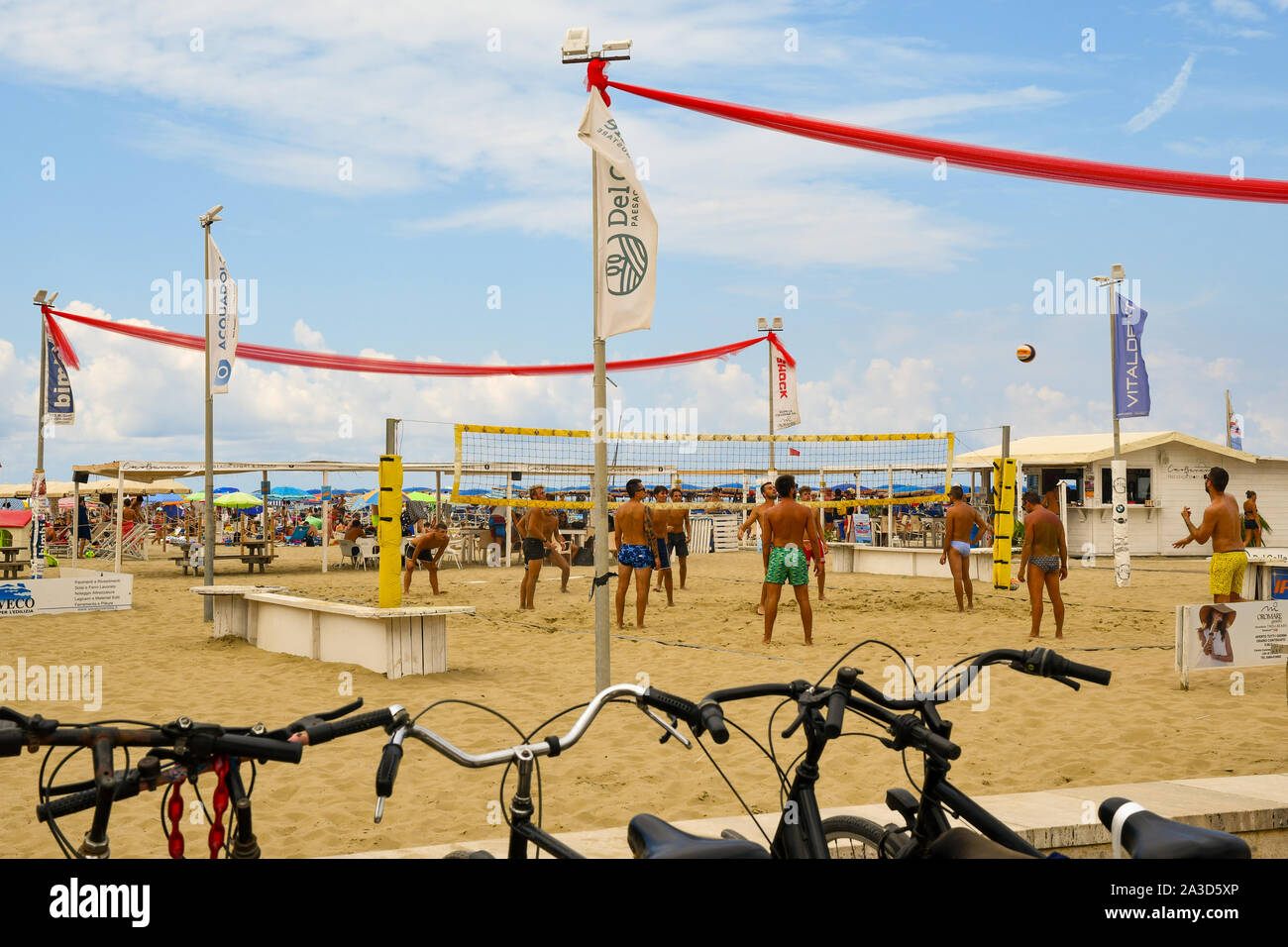 I giovani uomini a giocare a beach volley sulla spiaggia sabbiosa di Lido di Camaiore in una posizione soleggiata a metà agosto giornata con le biciclette parcheggiate, Versilia, Toscana, Italia Foto Stock