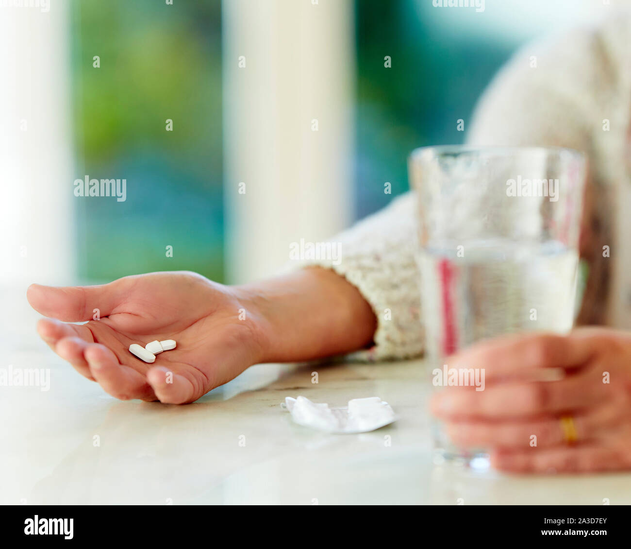 Donna che mantiene pillole con un bicchiere di acqua Foto Stock