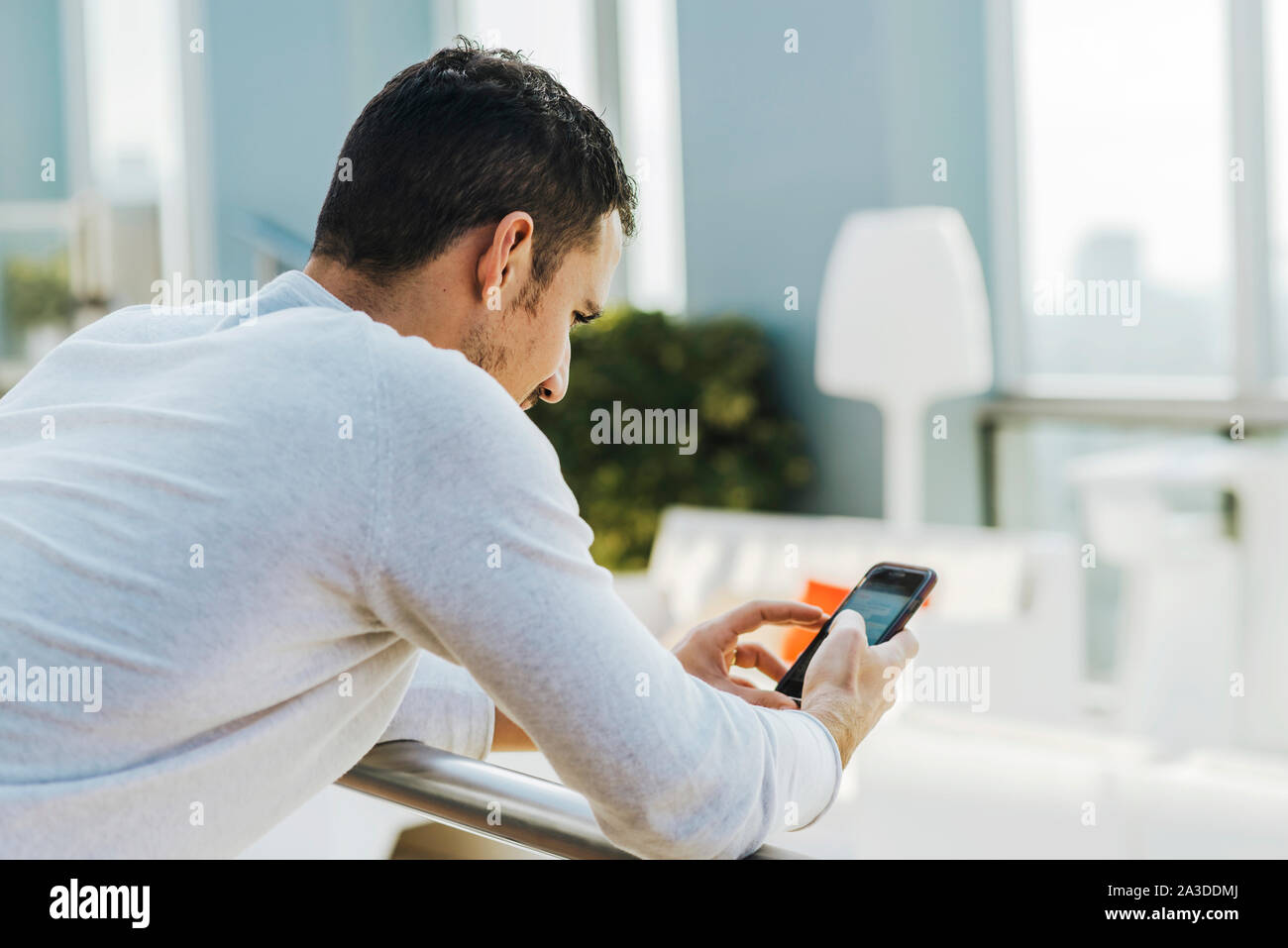 Giovane uomo appoggiato sulla ringhiera mentre si utilizza il telefono cellulare Foto Stock
