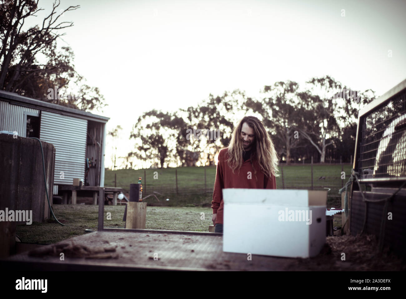 Bohemian uomo con i capelli lunghi e la barba sorride al tramonto in agriturismo Foto Stock