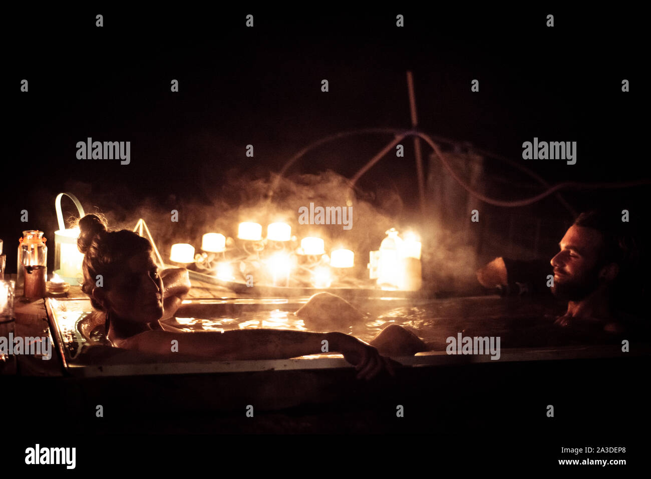 Coppia giovane sedersi nella vasca calda all'aperto durante la notte con romantiche candele Foto Stock