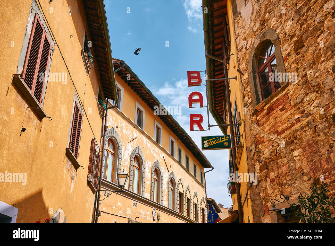 Basso angolo di barra rossa cartello sul lato dell antico edificio sulla strada stretta sotto il cielo blu in Toscana Foto Stock