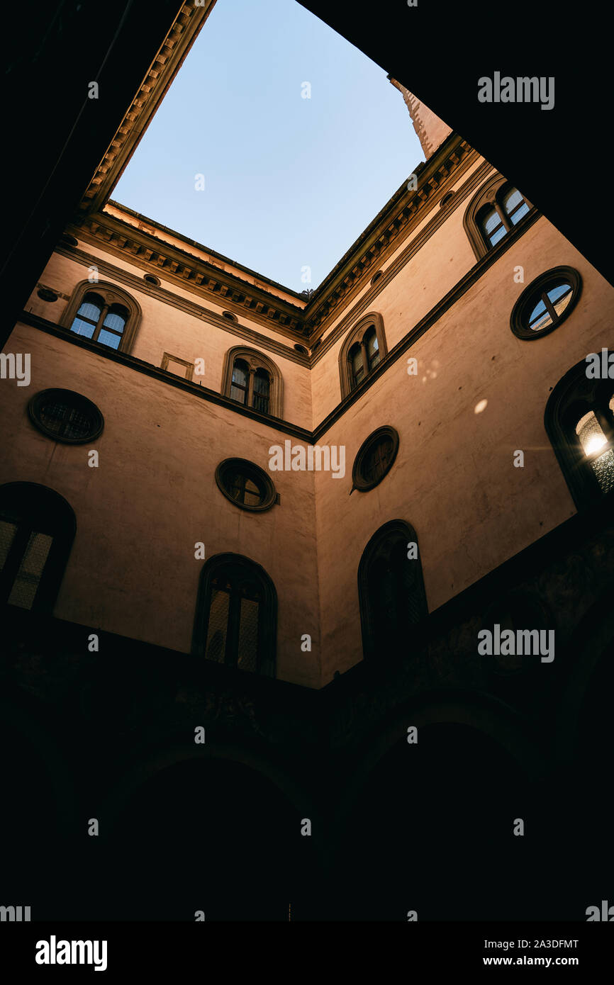 Da sotto il blu limpido cielo sopra il cortile scuro e un po' squallide pareti di edificio di età in Toscana, Italia Foto Stock