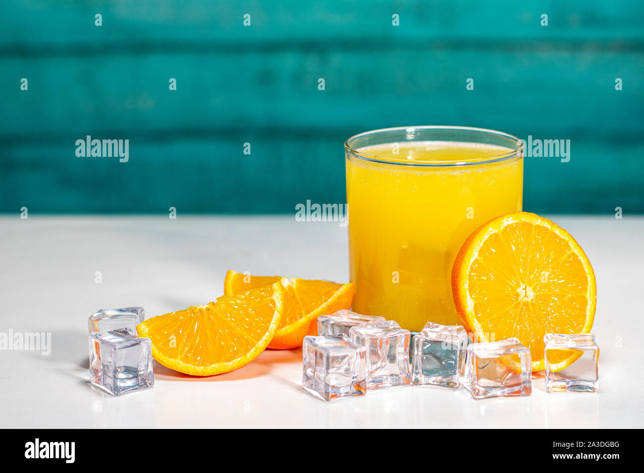 Bicchiere di succo di arancia e arance su un tavolo bianco e pareti in legno Foto Stock